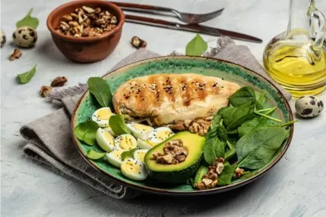 Assiette composée avec filet de poulet grillé, avocat, œufs de caille, épinards et noix