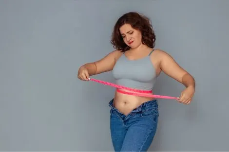 Femme mesurant son tour de taille avec un mètre ruban, illustrant les changements de silhouette