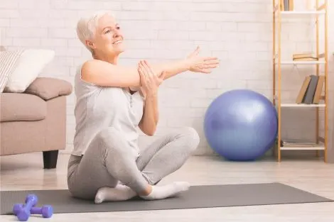 Femme assise sur un tapis de sport, s’étirant avec des haltères à proximité, exercice doux à domicile