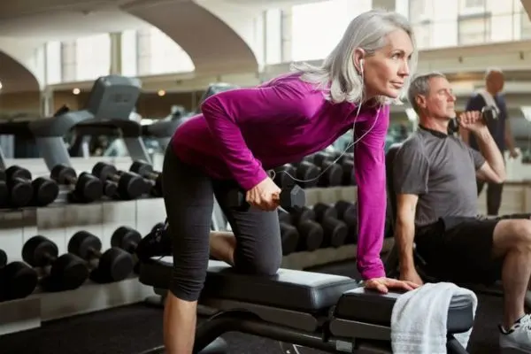 Femme senior faisant un exercice de musculation avec haltère sur banc en salle de sport