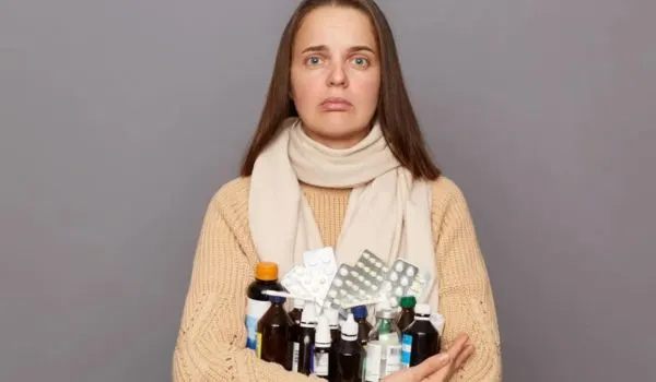 Femme inquiète tenant plusieurs boîtes et flacons de médicaments dans ses bras