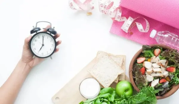 Réveil, salade et accessoires de sport sur fond blanc, illustrant une routine santé