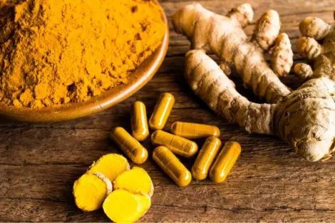 Poudre de curcuma, racines de curcuma et gélules de complément alimentaire sur une table en bois