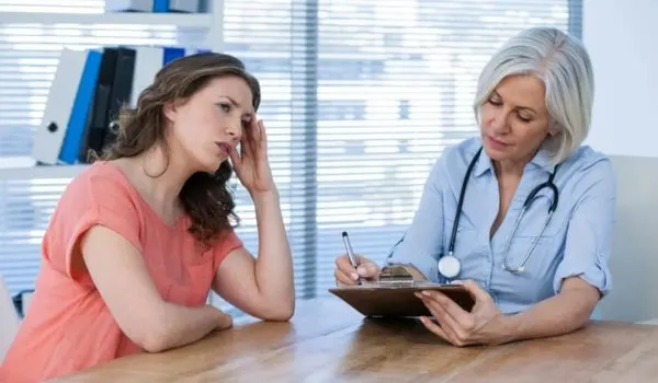 Médecin en consultation prenant des notes pendant qu’une femme explique ses symptômes
