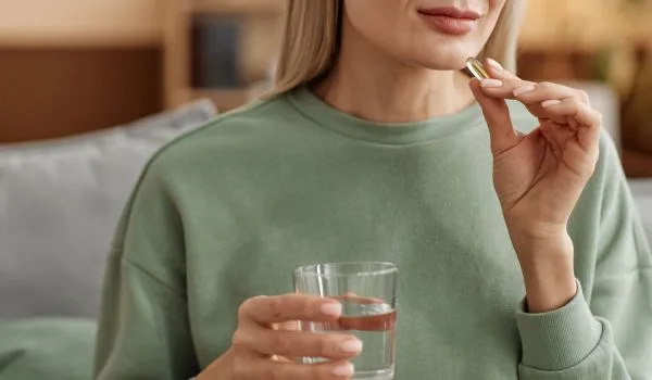 Femme assisetenant un verre d’eau et un complément alimentaire