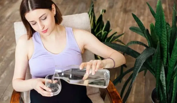 Femme enceinte assise versant de l’eau dans un verre, illustrant l’importance de l’hydratation