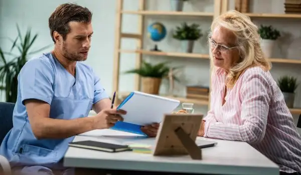 médecin en blouse discutant avec une patiente en cabinet, avec un support de type dossier/ordonnance, symbole d’une prescription encadrée