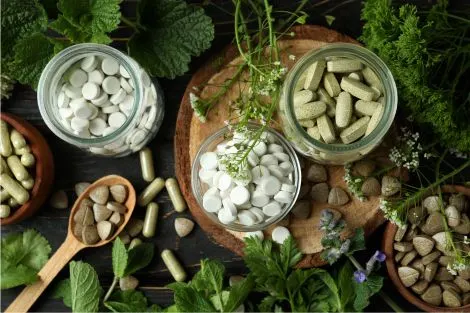 Compléments alimentaires naturels (gélules, probiotiques, plantes) sur une table en bois avec feuilles vertes