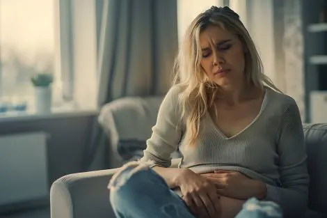 Jeune femme assise sur un canapé souffrant de douleurs abdominales,
signes de sécheresse vaginale