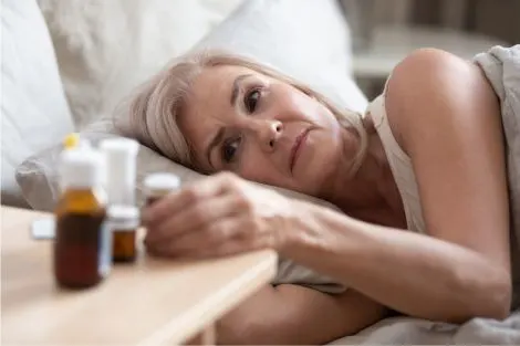Femme de 50 ans allongée regardant ses médicaments sur la table de nuit, lien entre ménopause et sécheresse vaginale
