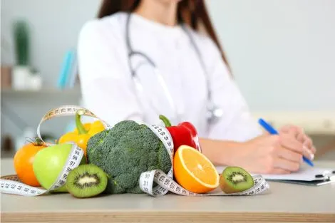 silhouette d'une nutritionniste, en train d'ecrire, sur la table mètre de ruban et fruits éxotiques.