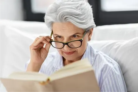 Femme âgée lisant un livre et ajustant ses lunettes