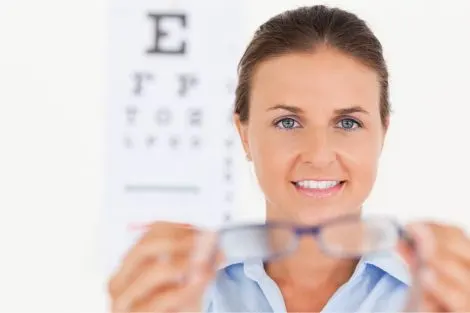 Une femme tient des lunettes devant un tableau optométrique lors d'un examen de la vue