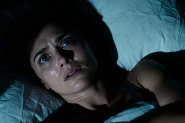 Personne anxieuse insomniaque dans son lit la nuit, yeux grands ouverts, en sueur, air préoccupé. Ambiance sombre et oppressante avec des jeux d'ombres symbolisant le stress mental et l'agitation intérieure.