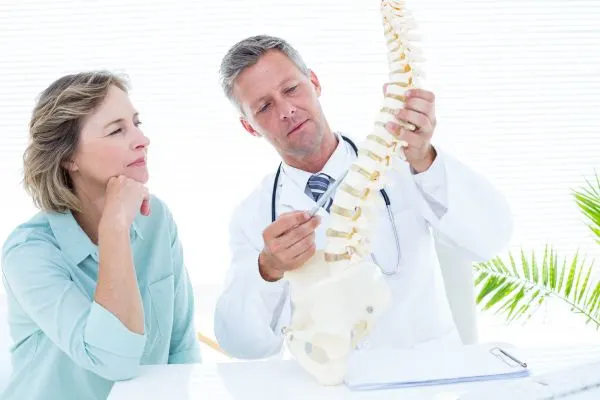 medecin montre a une patiente plus de 50 ans une colonne lombaire et les disques intervertébraux qui s'usent avec l'âge
