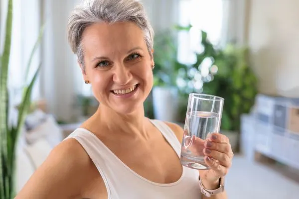 Femme de plus de 50 ans souriante avec un verre d’eau, symbolisant un cortisol mieux équilibré