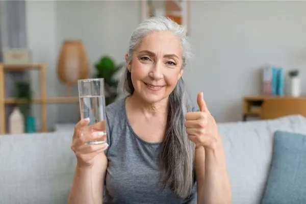 Senior sereine assise avec un verre d’eau a la main, illustrant le bienfait du jeûne hydrique après 50 ans