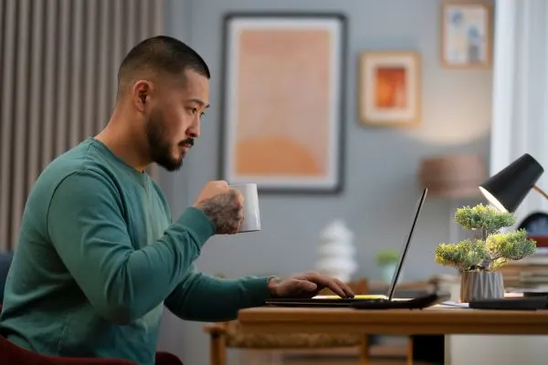 Homme devant un ordinateur avec café et notifications, symbole d’habitudes qui augmentent le cortisol