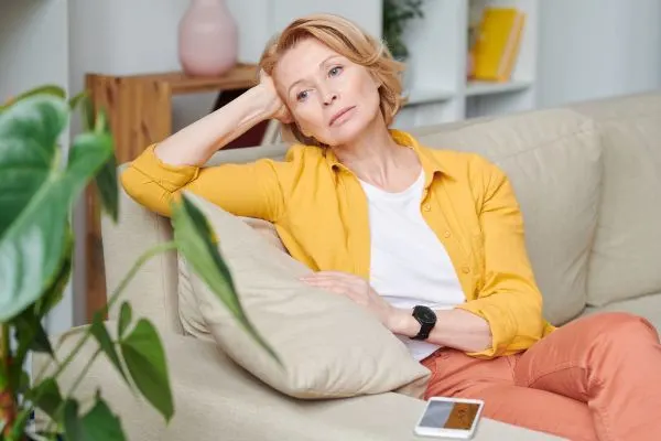 femme de 60 ans fatiguee et pensive assise sur un canape illustrant les symptomes d'un manque de serotonine