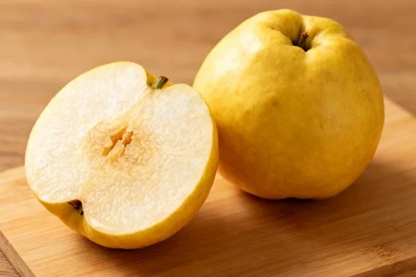 Coing jaune doré entier et coupé, montrant sa chair ferme et granuleuse sur une planche de cuisine