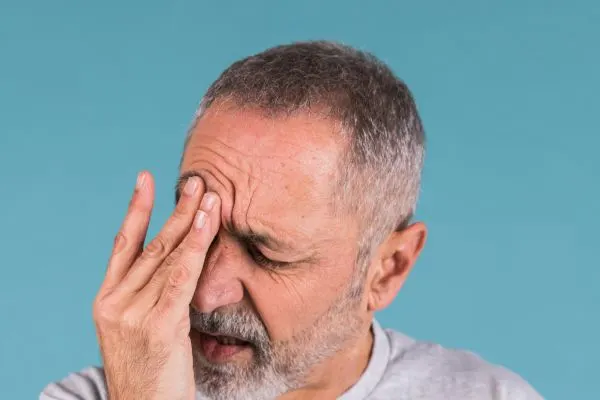 Homme senior assis, les yeux fermés, avec une douleur localisée au front et autour d’un seul œil