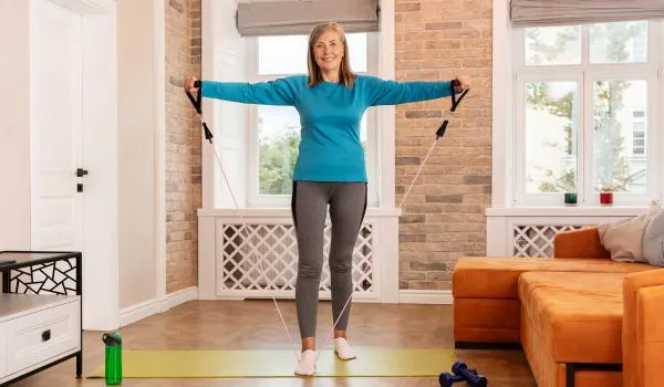 Femme senior utilisant une bande élastique rose pour renforcer ses bras et épaules à la maison