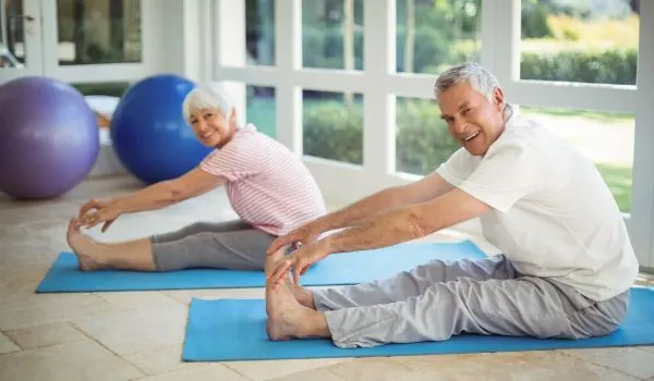 Couple senior souriant faisant des étirements au sol, image de bien-être et de santé préservée