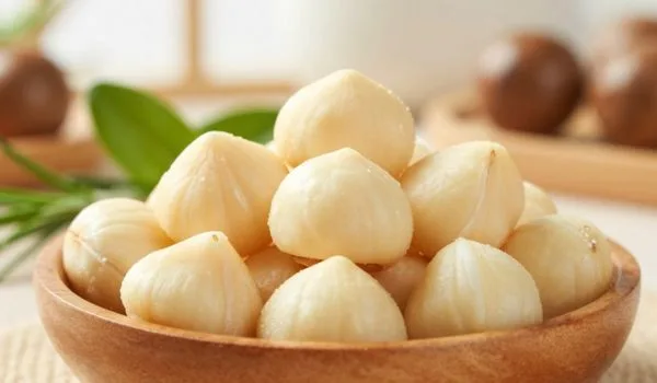 un bol en bois rempli de noix de macadamia. Les noix sont de couleur crème, lisses et ont une forme légèrement conique.
