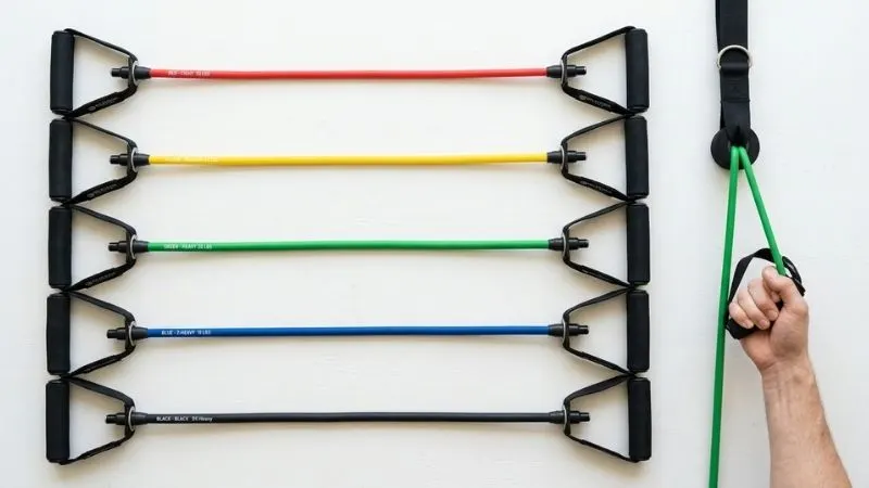 Présentation de plusieurs élastiques de résistance de couleurs différentes (rouge, jaune, vert, bleu, noir)
disposés avec poignées, sur fond clair.