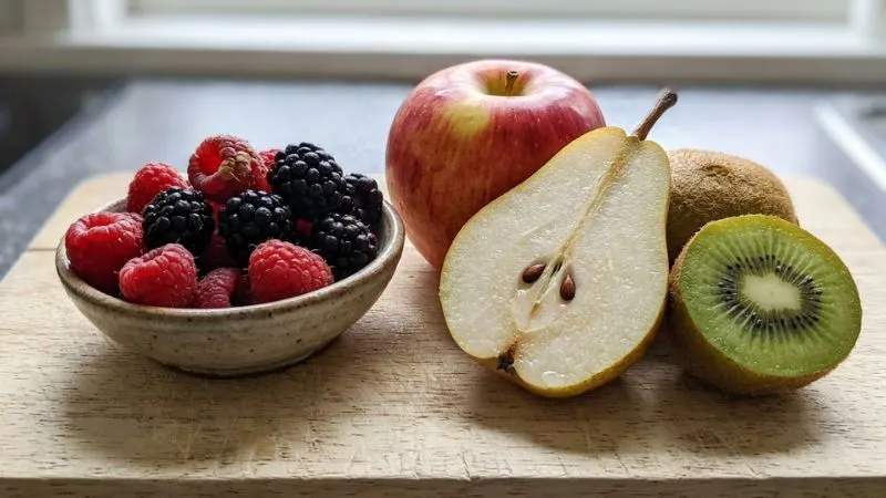 gros plan sur une sélection de fruits fibreux, avec une poire coupée, une pomme avec sa peau, des framboises,
des mûres et un kiwi